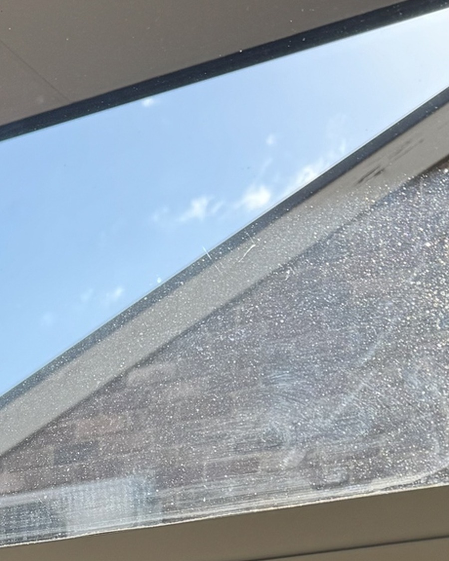 Close-up of a window roofline view before OniClean coating, glass hazy with dust and residue almost hiding the house behind it